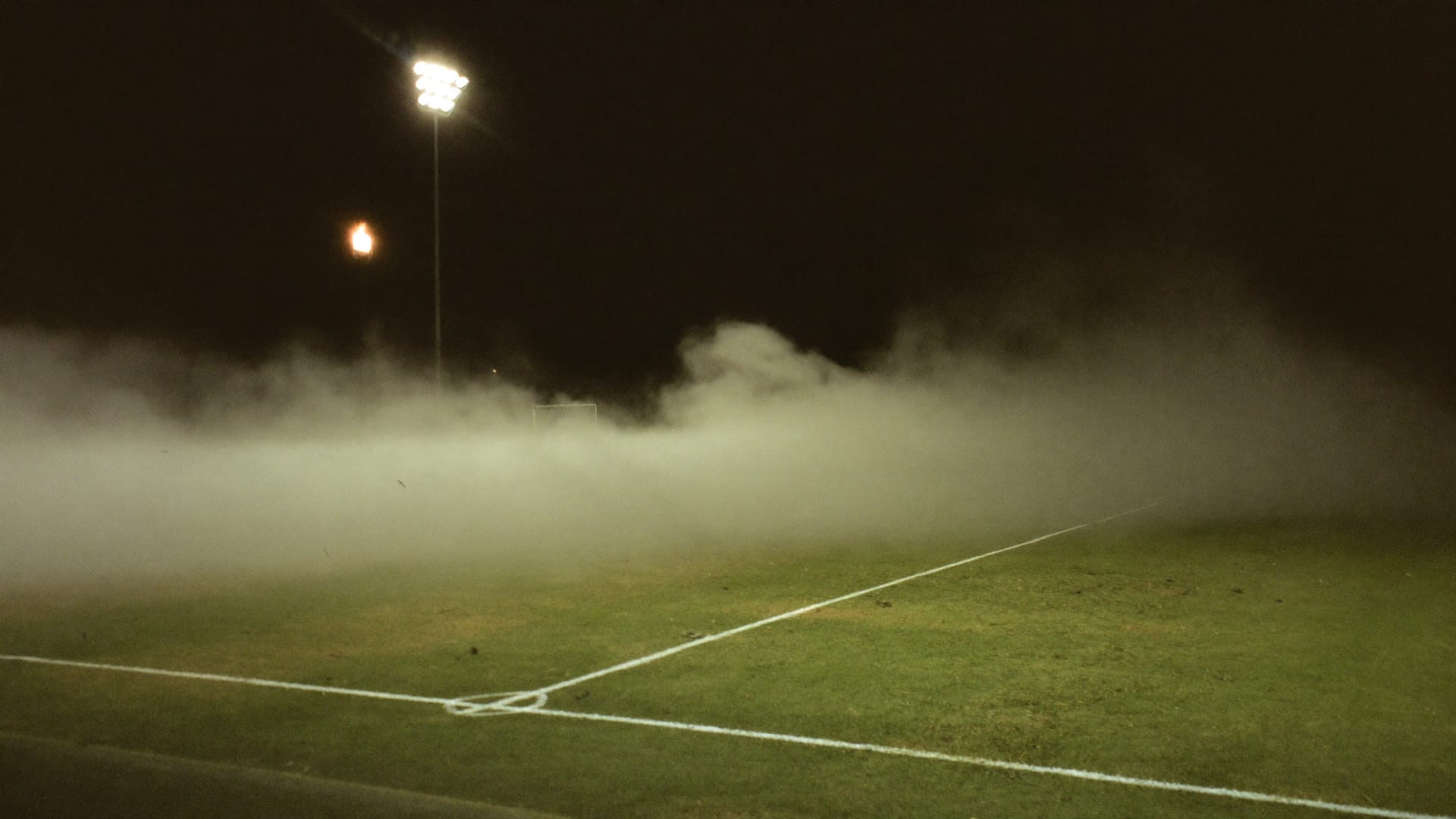 Fog drifting across an empty floodlit pitch after the final whistle.